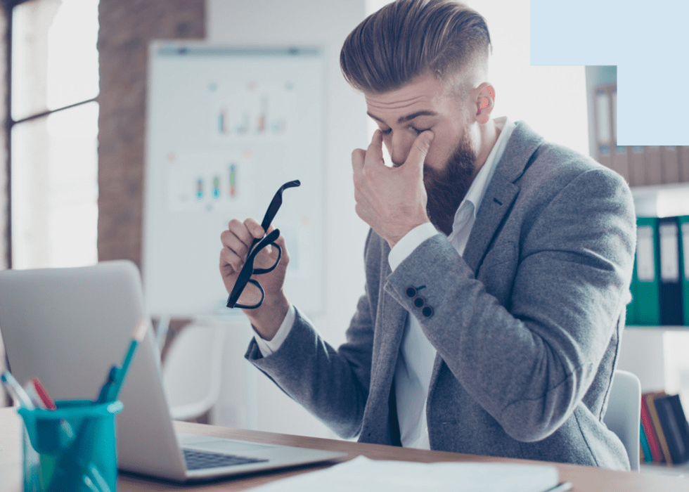 Un homme assis devant un ordinateur portable se frotte les yeux